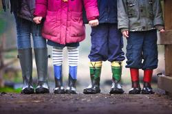 Beine von vier Kindern mit schlammigen Regenstiefeln