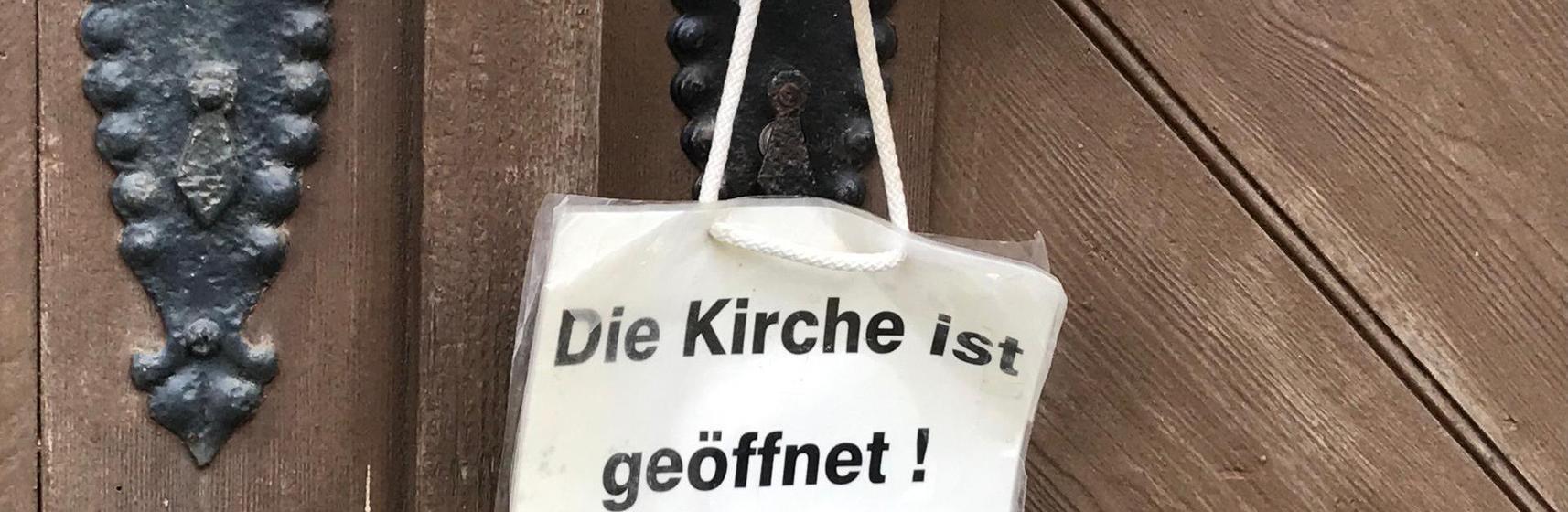 Kirchentür mit Schild "Die Kirche ist geöffnet"
